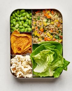 a lunch box filled with vegetables, rice and crackers on top of lettuce