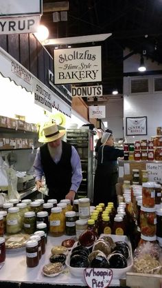 a man standing in front of a counter filled with jars of honey and jams