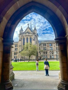 two people standing under an archway in front of a large building with a clock tower