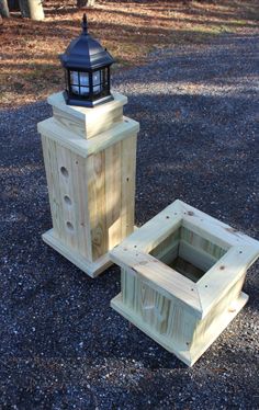 two wooden boxes sitting on top of gravel next to a light house in the woods