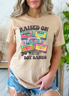 "Attention all 90s pop aficionados! If you grew up on a steady diet of Backstreet Boys, N'SYNC, and other iconic boy bands, then this graphic tee is a must-have for your wardrobe. Featuring retro cassette tapes adorned with the names of your favorite 90s heartthrobs, this tee is a true throwback to the golden era of boy bands. Crafted from high-quality, soft cotton, this \"Raised on 90s Boy Bands\" tee is the perfect blend of comfort and style. Whether you're running errands or reliving your glory days with a nostalgic playlist, this tee is sure to make a statement and turn heads. Targeting women who were raised in the 90s, this tee is the perfect way to relive those cherished memories of singing along to your favorite boy band hits with your best friends. So why wait? Click the link and a Nostalgic Playlist, 90s Graphic Tees Vintage, 90s Tshirts, 90s Heartthrobs, 90's Outfit, Band Tee Outfits, 90s Boy Bands, Retro Shirt Design, Boyz Ii Men