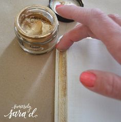 a woman's hand is touching the bottom of a jar of gold colored powder