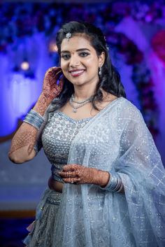 a woman in a blue dress and jewelry smiling at the camera with her hands on her face