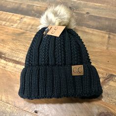 a black beanie with a white pom - pom on the top and a tag attached to it