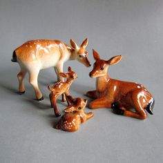 three ceramic deer and two fawns on a gray surface with one laying down