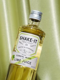 a bottle of lime juice sitting on top of a green cloth covered table next to a curtain