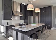 a large kitchen with black cabinets and white counter tops, two pendant lights over the island