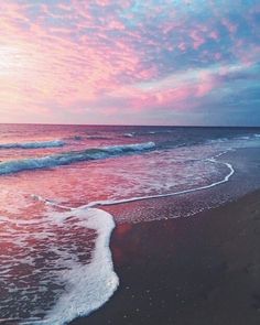 an ocean beach with waves coming in to the shore and pink clouds above it at sunset