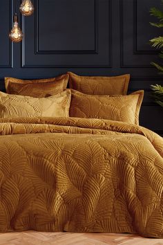 a bed with gold comforter and pillows in a room next to a potted plant