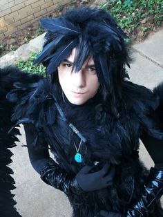 a man dressed in black with feathers on his head and gloves, posing for the camera