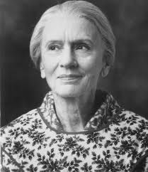 an old photo of a woman with white hair and black flowers on her shirt, looking at the camera