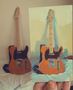 someone holding up a painting of an electric guitar and a miniature guitar in front of them