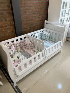 a white crib with pink and gray bedding in a room next to a brick wall