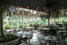 an empty restaurant with tables and chairs in front of large windows filled with potted plants