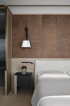 a white bed sitting next to a night stand and lamp on top of a wooden wall