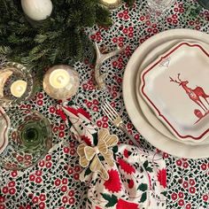 a christmas table setting with red and white napkins, silverware, candles and evergreen branches