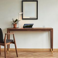 a wooden desk with a laptop on it next to a black chair and framed photograph