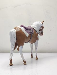 a small toy horse with a saddle on it's back, standing in front of a white wall