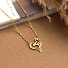 a gold necklace with a musical note in the shape of a heart on top of a book