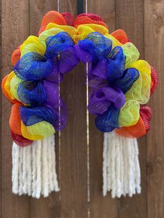 a multicolored mesh wreath hanging on a wooden fence with tassels around it