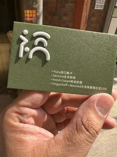 a person holding up a green business card with white letters on it in front of a brick building