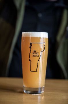 a glass filled with beer sitting on top of a wooden table next to a person