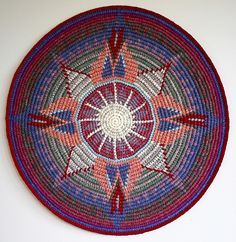 a circular woven rug with red, white and blue designs on the center is hanging on a wall