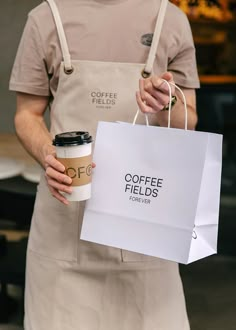 a man in an apron holding a coffee bag and a paper cup with the words coffee fields printed on it