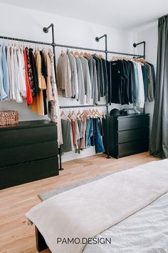 an organized closet with clothes hanging on the rail and bed in front of it,