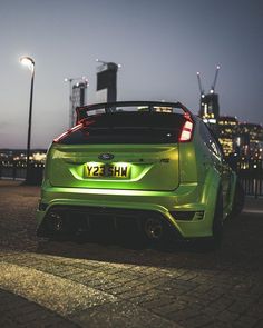 the back end of a green car parked in front of a city skyline at night