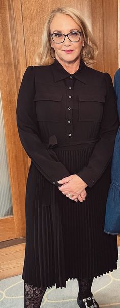 a woman wearing glasses standing in front of a wooden door with her hands on her hips