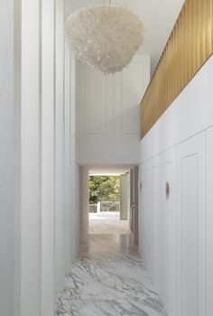 a hallway with white walls and marble flooring is lit by a chandelier hanging from the ceiling