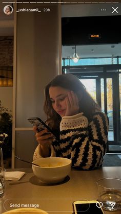 a woman sitting at a table looking at her cell phone and mixing something in a bowl