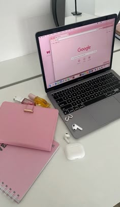 an open laptop computer sitting on top of a white desk next to a pink binder