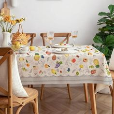 a dining room table covered with a white table cloth and fruit design on it, next to two chairs