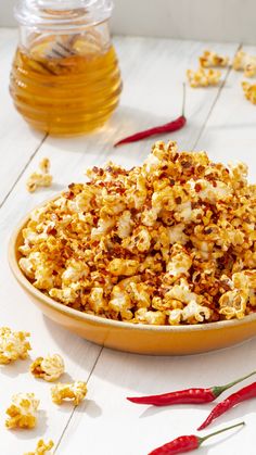 a bowl filled with popcorn sitting on top of a table next to chili peppers and honey