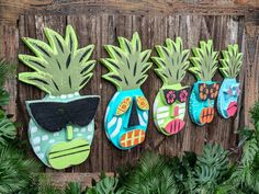 three colorful pineapples are hanging on a wooden fence with green plants around them