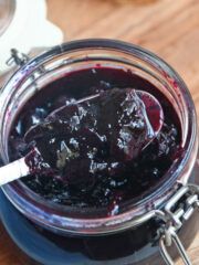 a jar filled with blueberry jam sitting on top of a wooden table next to a spoon