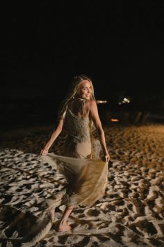 a woman is walking on the beach at night with her dress blowing in the wind