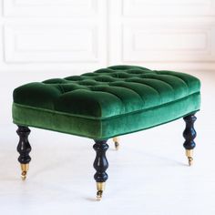 a green velvet footstool with gold trimmings on the legs and feet