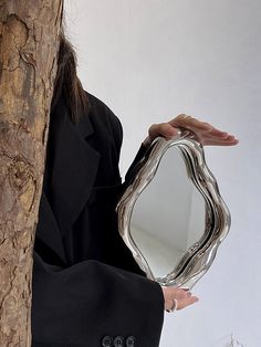 a woman holding a mirror in front of her face while standing next to a tree