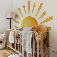 a baby's room with a crib and sun painted on the wall behind it