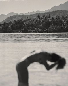 a person standing in the water with their head above his body and mountains in the background