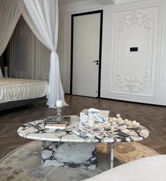 a white bed sitting next to a table on top of a hard wood floor in a bedroom