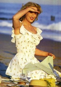 a woman is sitting on the beach with her hat in her hand and looking at the camera