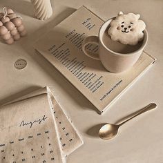 a cup of coffee on top of a table next to an open book and spoon