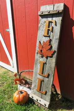 a wooden sign sitting next to a red barn with pumpkins on the grass in front of it