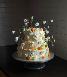 a large white cake with orange and white flowers on it sitting on top of a table