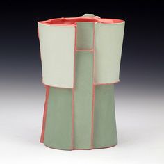 a white and green vase with pink trim on it's sides, sitting on a table