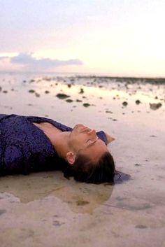 a woman is laying on the beach with her head in the water and eyes closed